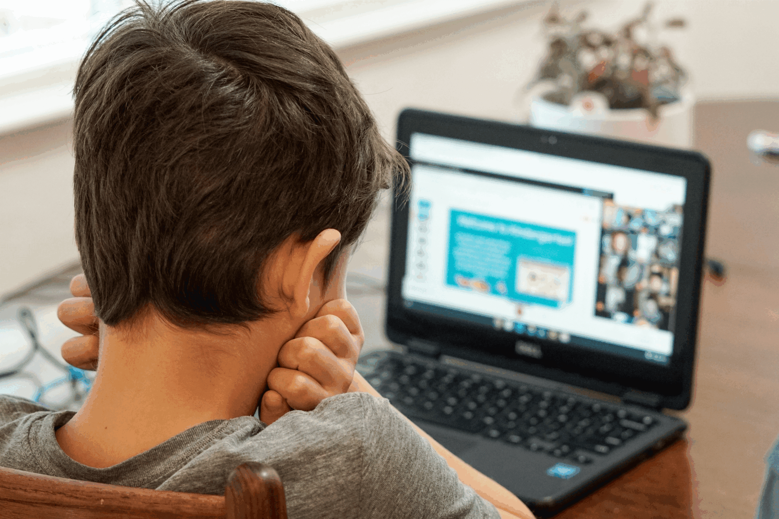 Boy watching online class on Dell laptop, wearing a gray shirt.