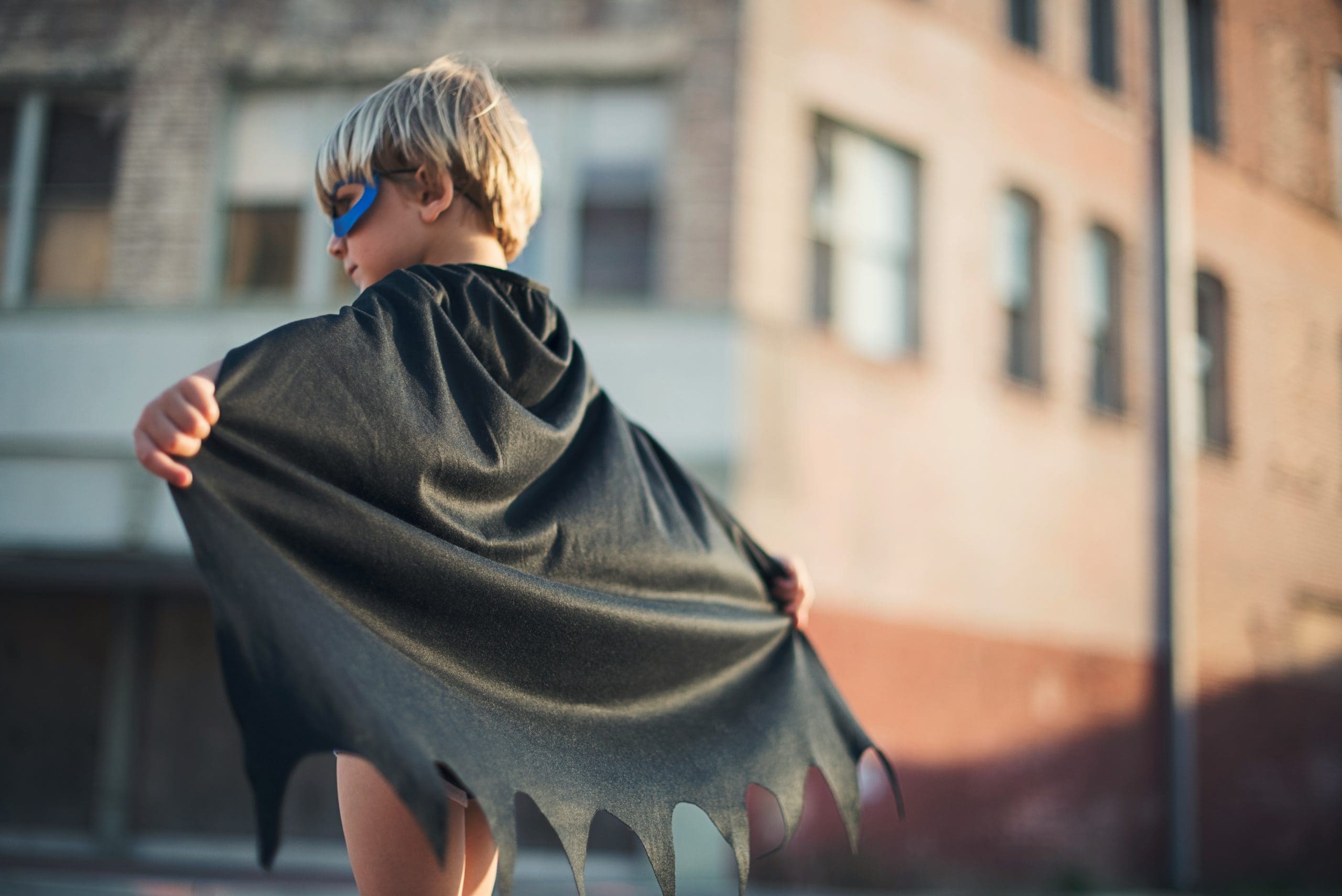 Child wearing a black cape and blue mask, standing outdoors, photo.