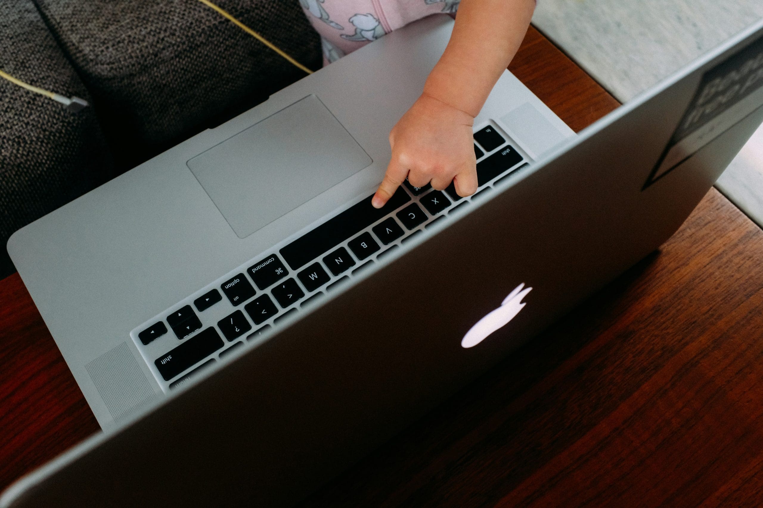 Child's finger pressing laptop keyboard, silver and black, photo, glowing logo.