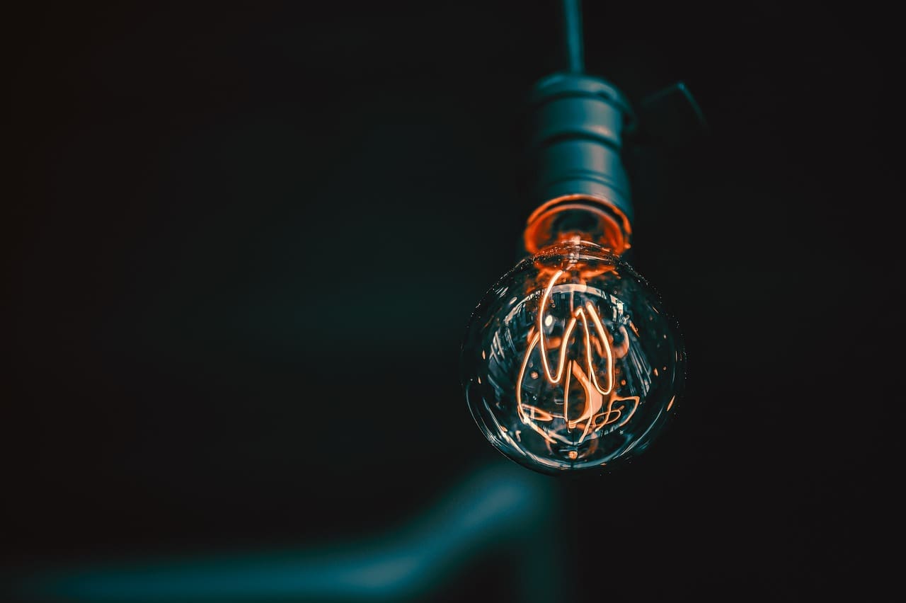 Close-up of glowing light bulb with orange filament, dark background, photo.