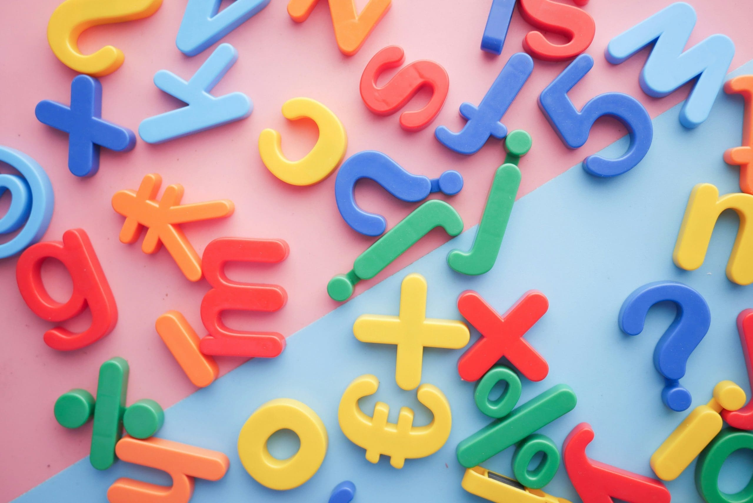 Colorful plastic letters and symbols scattered on pink and blue background.