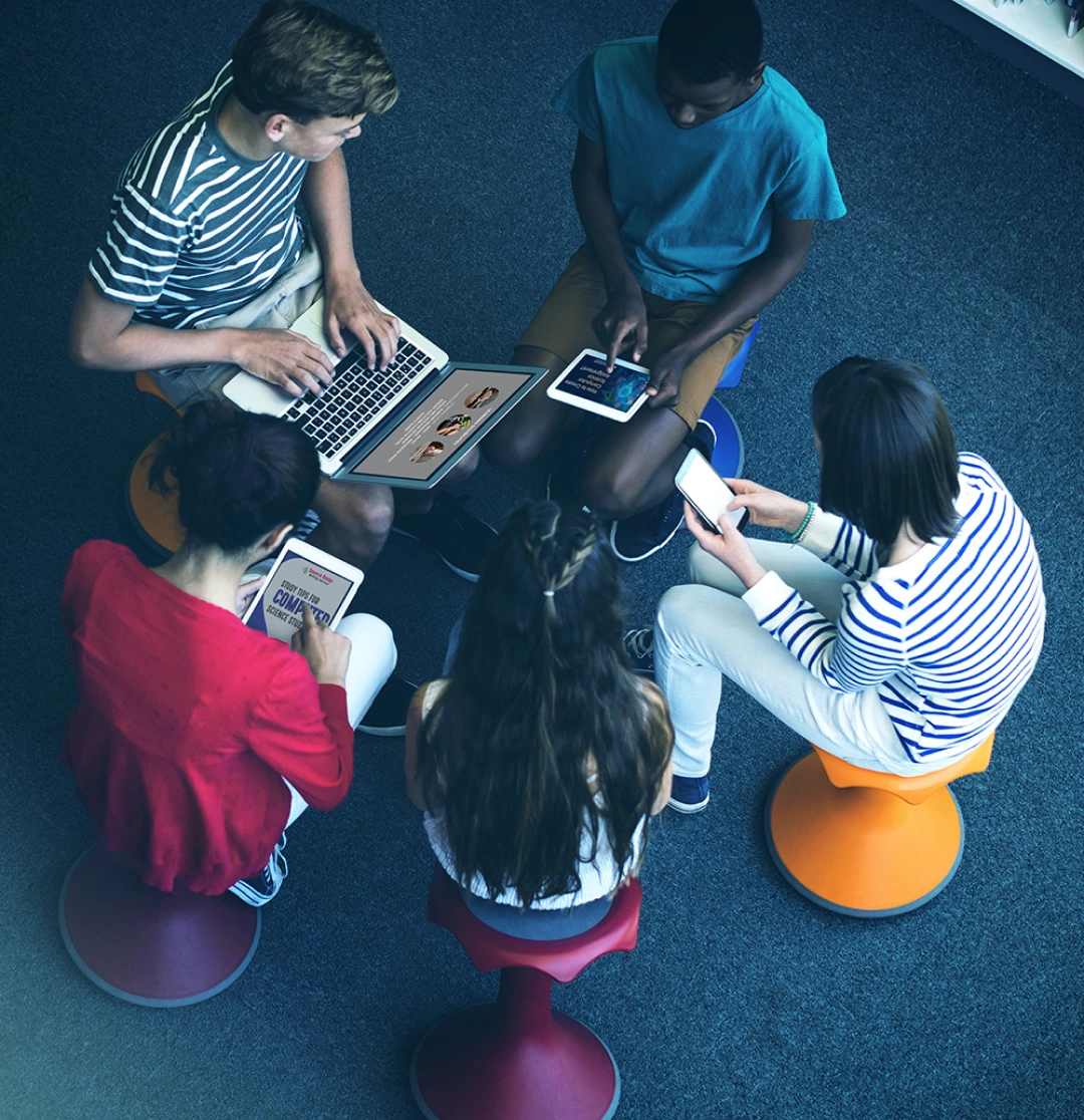 Five people using devices in a circle, colorful seating, overhead photo.
