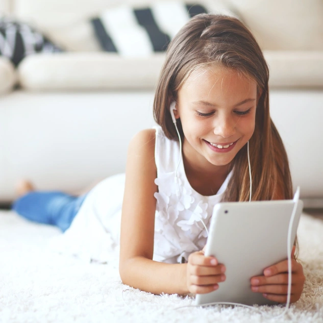 Girl smiling while using tablet, wearing white, in bright indoor photo.