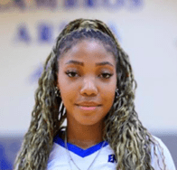Person with braided hair wearing a white jersey, photographed indoors, blurred text.
