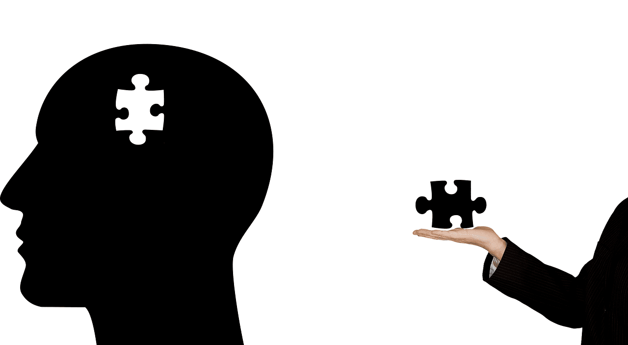 Silhouette head with puzzle piece, hand holding piece, black and white illustration.
