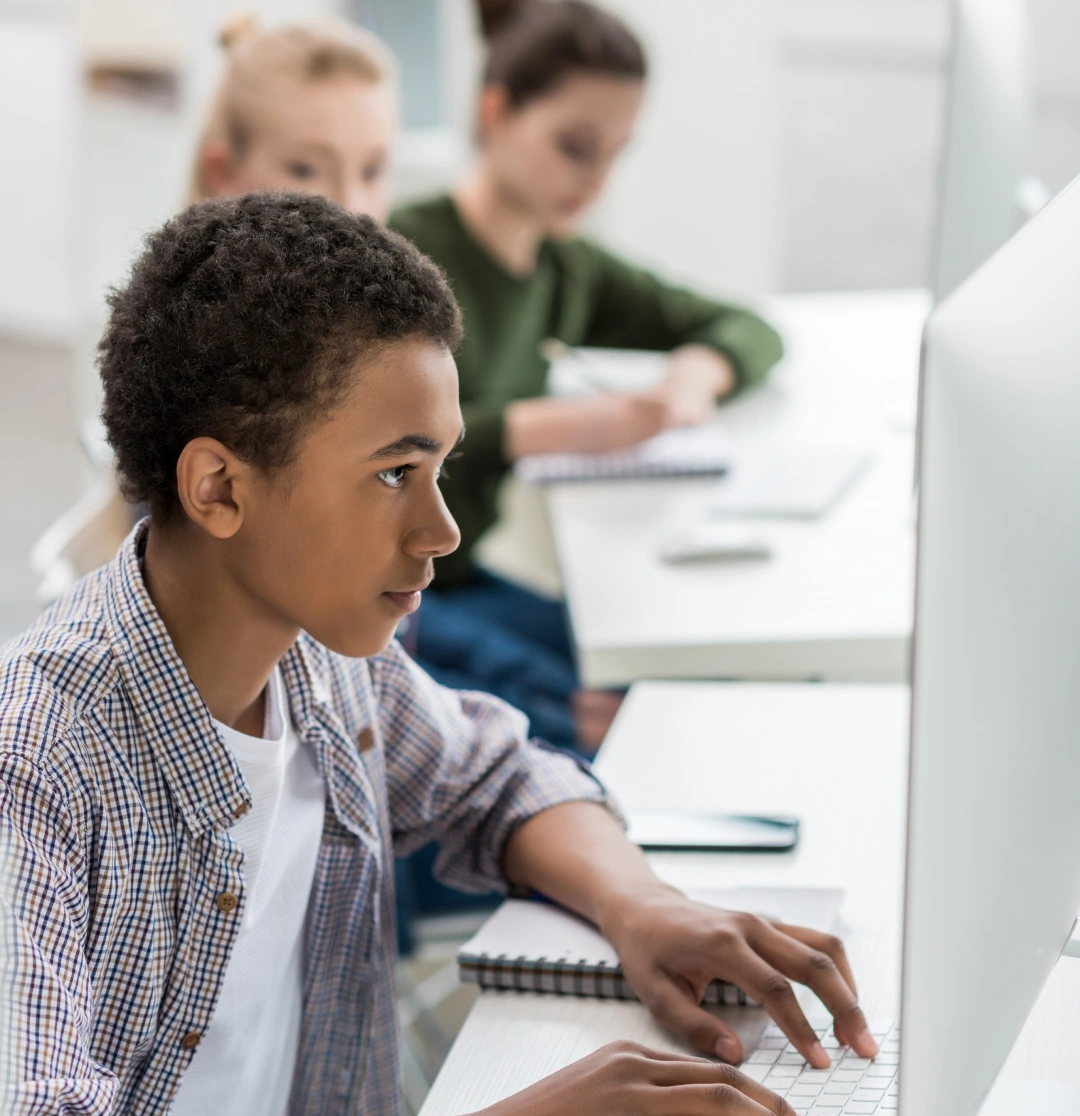 Student typing on a computer in classroom, wearing plaid shirt, photo.