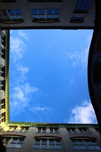 Upward view of building courtyard framing blue sky with scattered clouds.