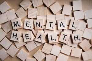 Wooden tiles spelling "MENTAL HEALTH" on scattered blank tiles, photo style.