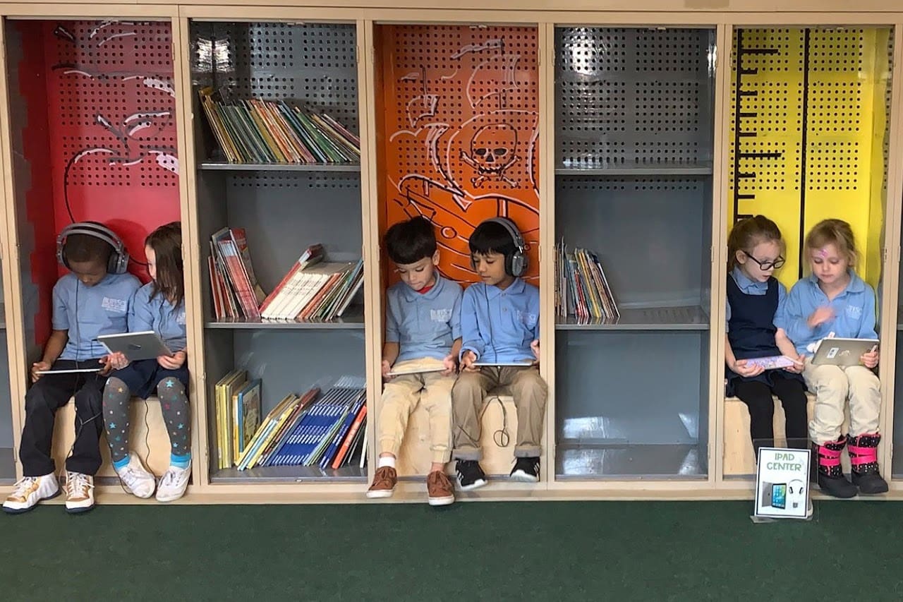 Children using tablets in colorful library cubbies, photo, "iPad Center" sign visible.