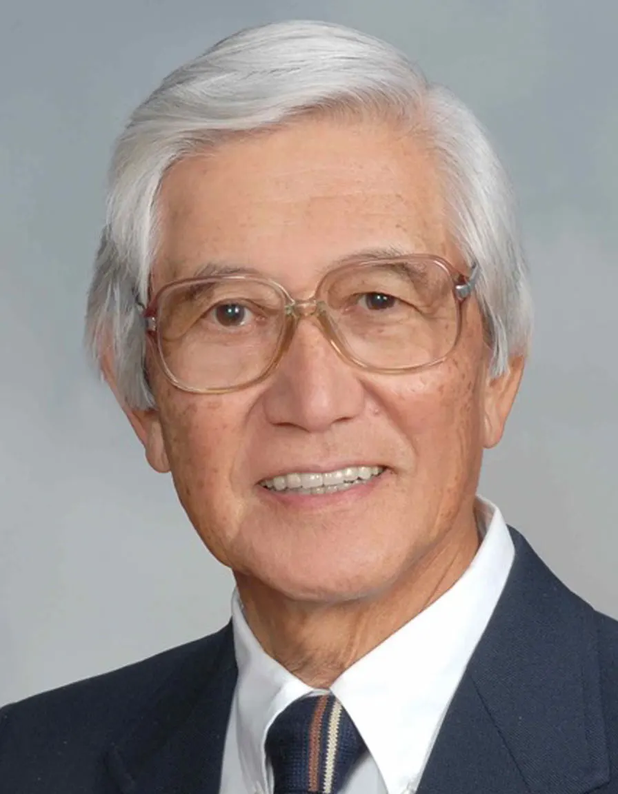Elderly man smiling, wearing glasses and suit, against gray background, photo.