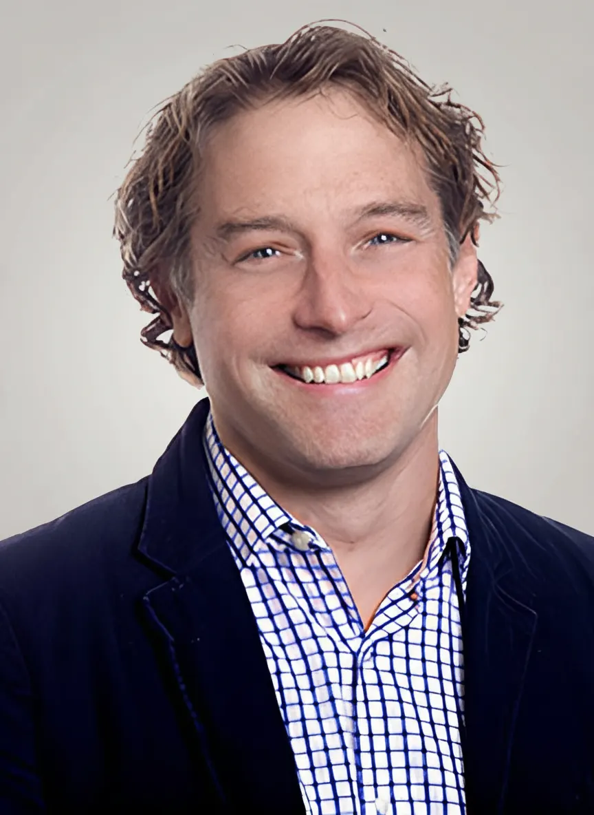 Smiling man in a blue jacket and checkered shirt, studio photo.
