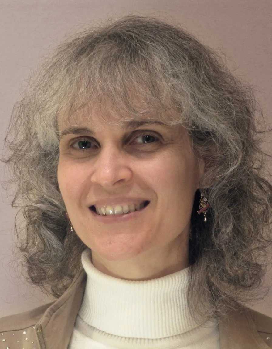 Smiling woman with gray hair, wearing white sweater, portrait photo style.