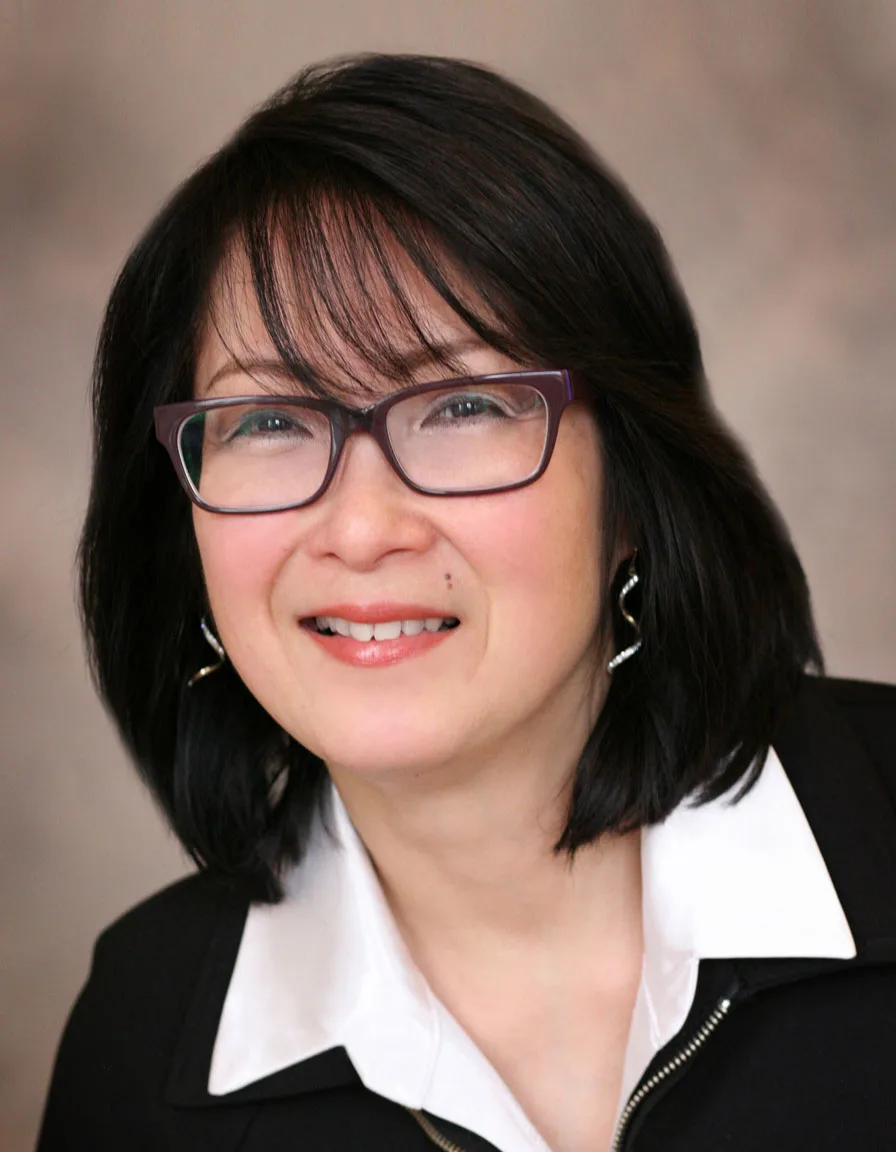 Woman smiling, wearing glasses, black jacket, white shirt, studio portrait photo.