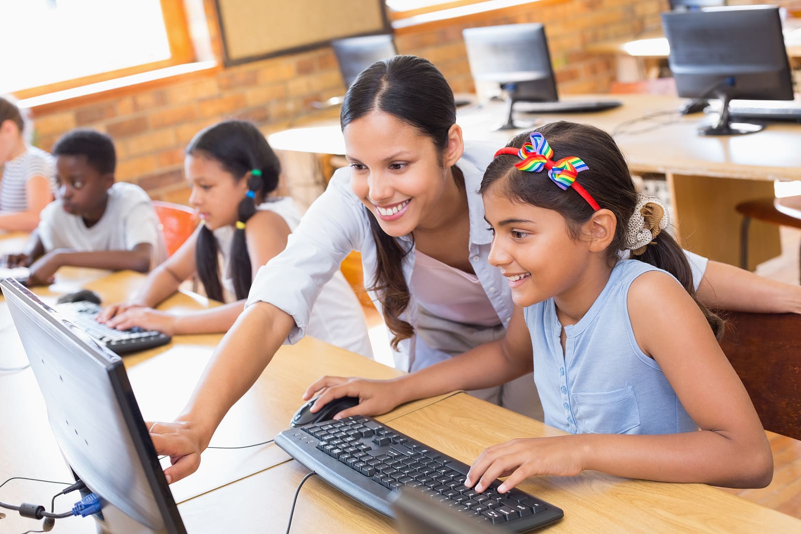 Smiling teacher helping a young student at a computer in a school computer lab